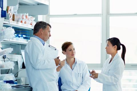 Tre personer diskuterar i ett labb
